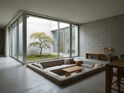 Minimal concrete house living room in Japan with a sunken seating area and a courtyard tree visible through glass, calm
